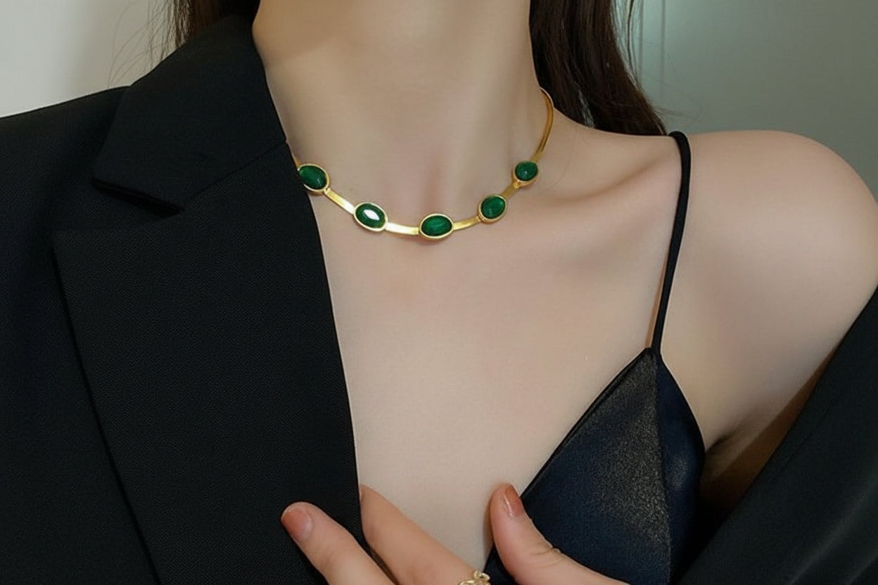 Gold necklace with green stones worn by a person in a black outfit.