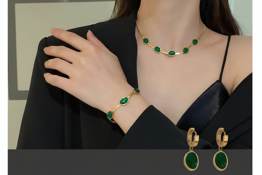 Gold jewelry set with green gemstones including necklace, bracelet, and earrings on a person wearing a black top.
