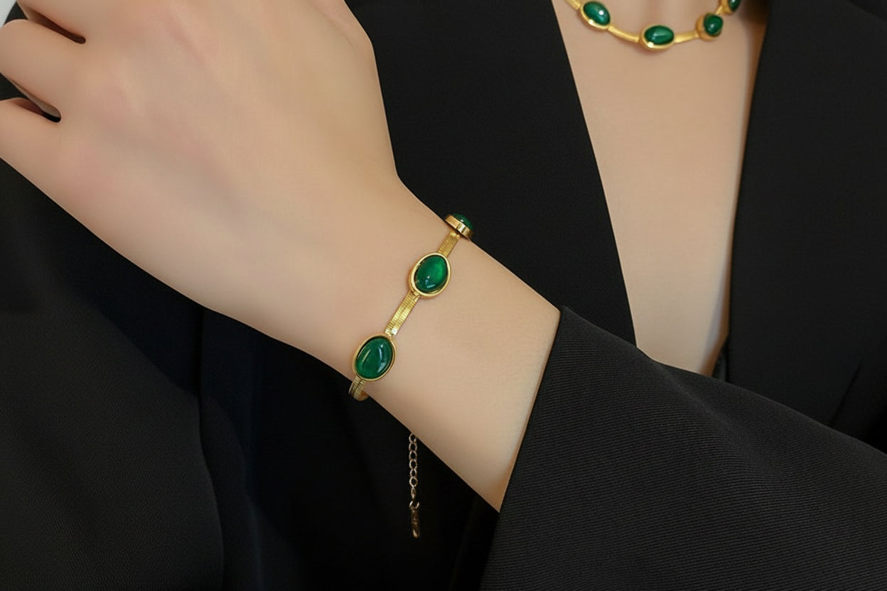 Gold bracelet with green stones on a wrist, worn by a person in a black outfit.